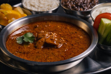 A thali platter with butter chicken, fruit, rice, daal, yogurt, tomato and cucumber.