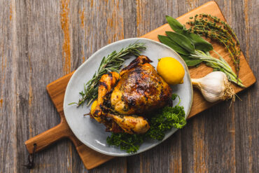 An overhead shot of roast chicken with fresh rosemary, sage, thyme, parsley, lemon and garlic.